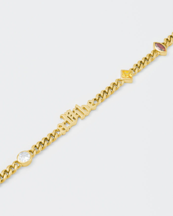 detail of A Vibe cuban chain bracelet with 18kt yellow gold coating, mixed shape bezel stones in diamond white, yellow, garnet, tanzanite and "A Vibe" central metal tag. Lobster clasp with logo
