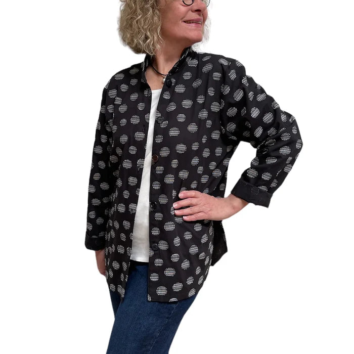 Person wearing a black patterned shirt over a white top with blue jeans on a white background
