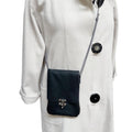 Black leather crossbody bag worn over a light gray coat on a white background