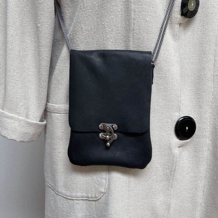 Black crossbody bag on a light gray coat with a plain background