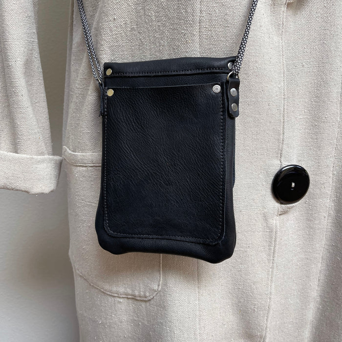 Black leather crossbody bag on a person wearing a light gray jacket.