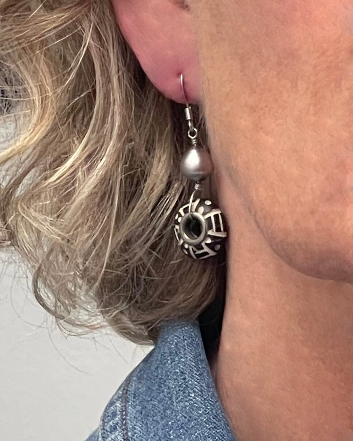 Close-up of a person wearing a silver hoop earring with a decorative pendant.