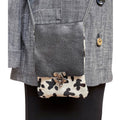 Gray textured handbag with cow print flap over a gray coat