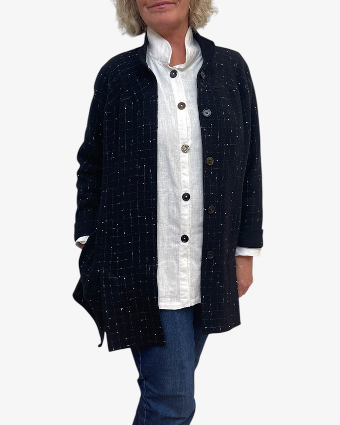 Person wearing a navy blue checkered jacket over a white shirt with rolled-up sleeves on a white background