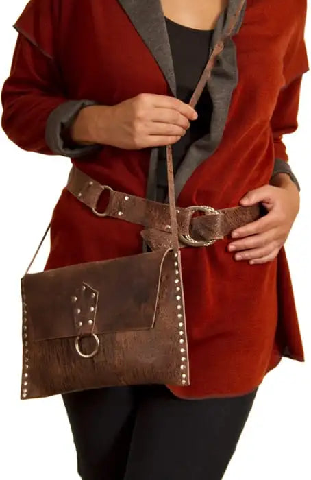 Person wearing a red coat holding a brown leather bag with a belt buckle.