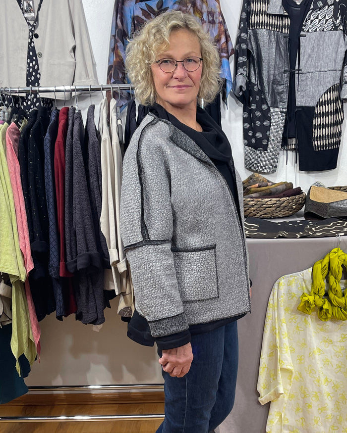 Woman standing in a clothing store with racks of clothes and shoes in the background.