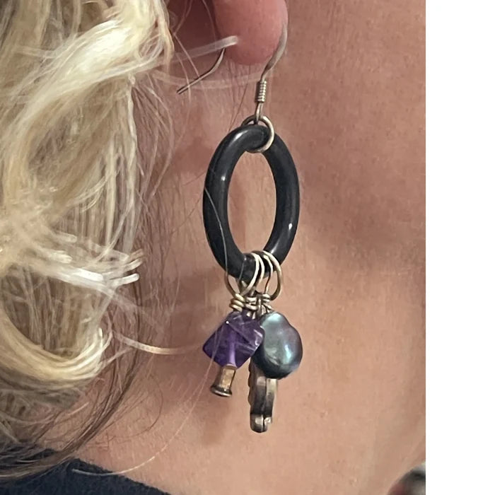 Close-up of a black hoop earring with beads held against skin.