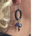 Close-up of a black hoop earring with beads held against skin.