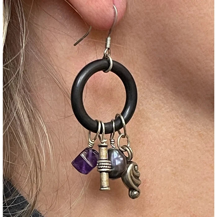 Close-up of an earring with black ring, purple bead, and gold accents on a person's ear.