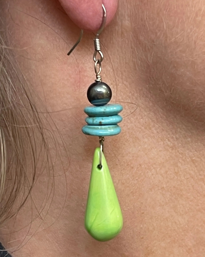 Earring with turquoise beads and a green teardrop pendant on skin.