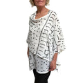 Woman wearing a white poncho with black geometric patterns on a white background