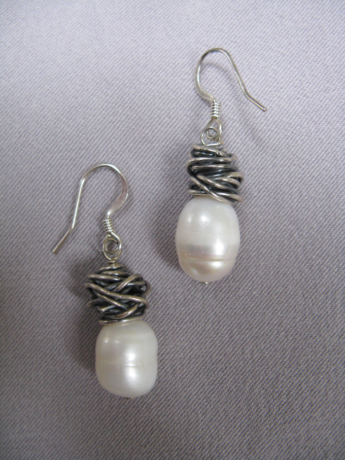 Pearl earrings with silver wire wrapping on a gray background