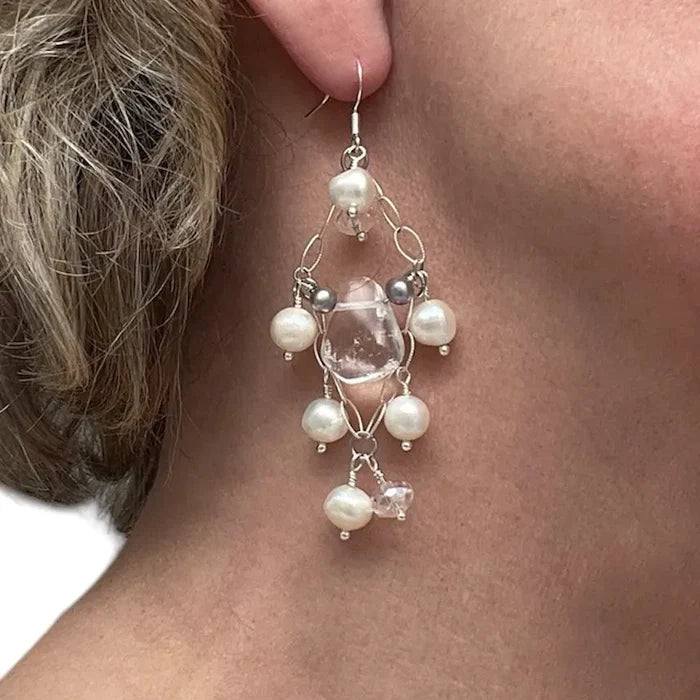 Close-up of a person wearing a decorative earring with pearls and a clear stone.